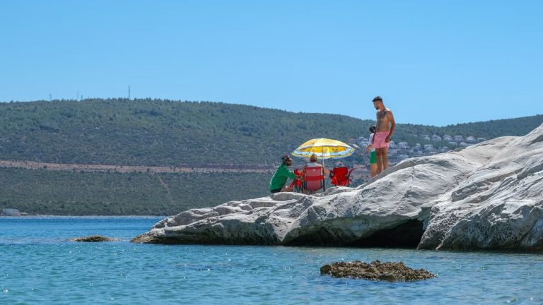 A group of people relaxing on rocky shore under a colorful umbrella on a sunny day