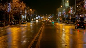 A city street at night with festive holiday lights reflecting on the wet road.